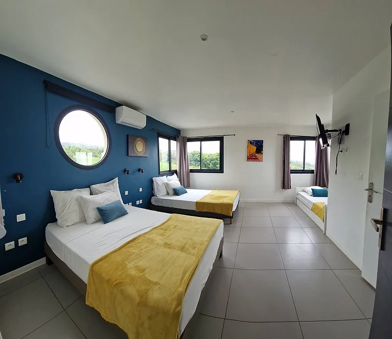 Une chambre au mur bleu, un lit double, un lit gigogne et une fenêtre ronde