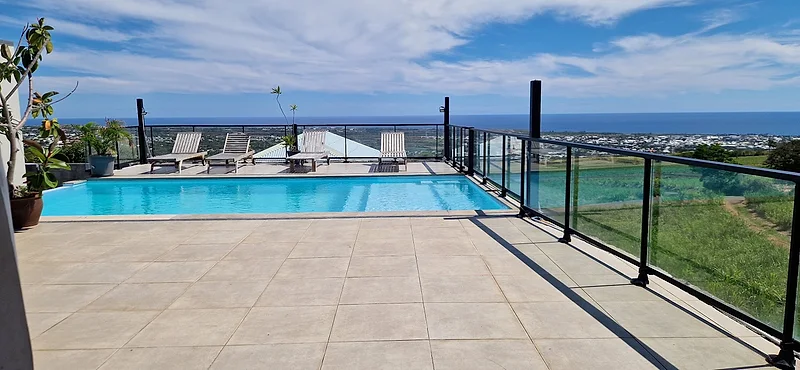 La terrasse dallée au bord de la piscine, l'océan au fond