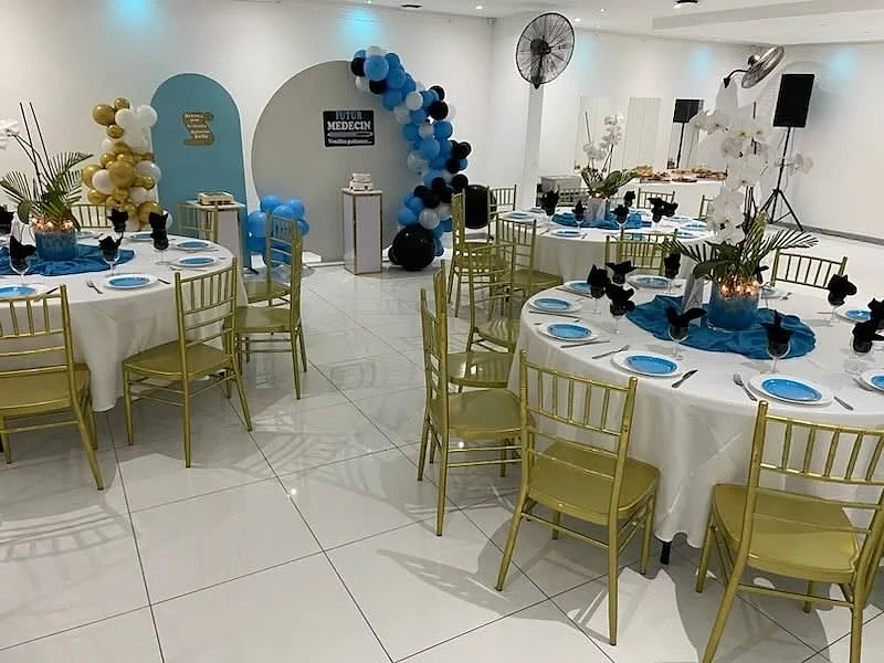 Des tables rondes aux chaises dorées, nappes bleues et ballons pour une fête