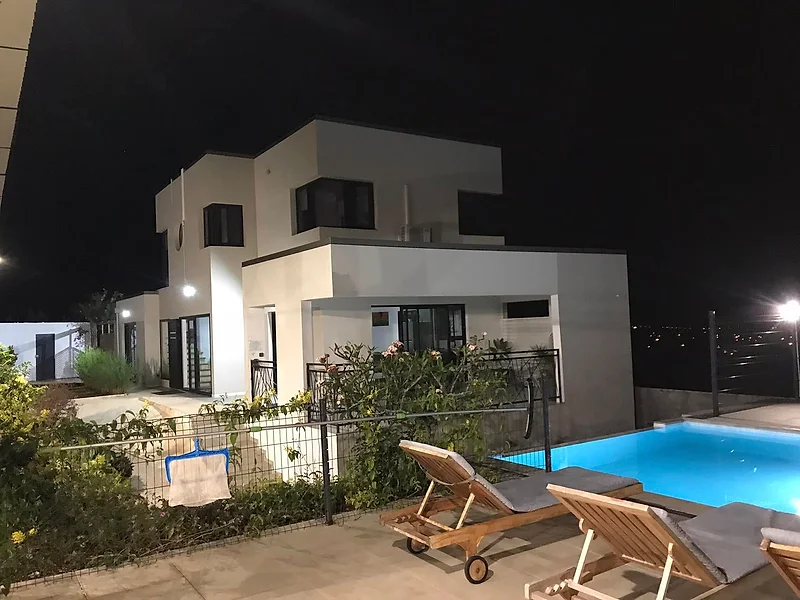 La villa la nuit, la piscine allumée et les transats